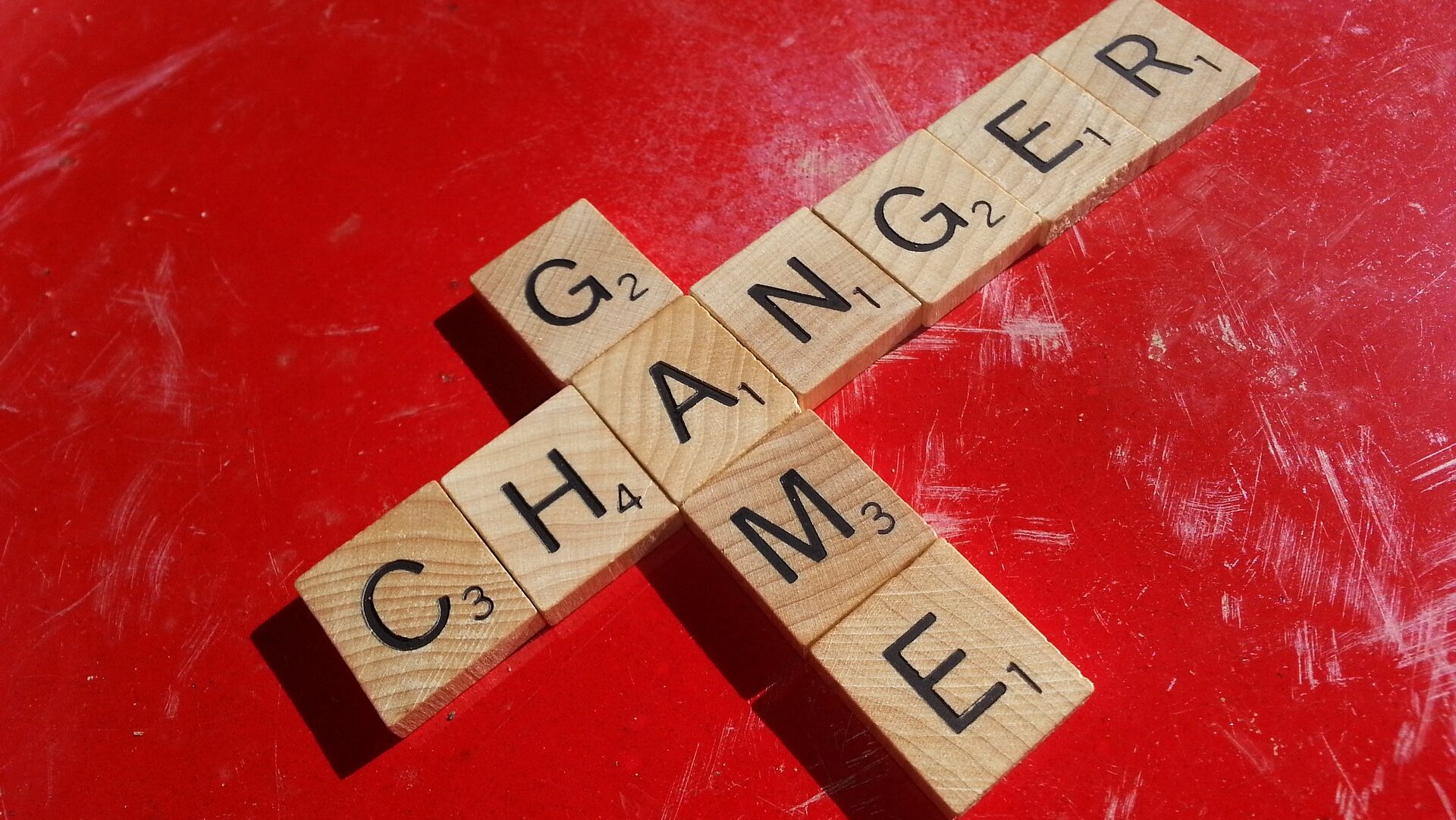Scrabble letters spelling "Game changer" in a perpendicular pattern sharing the letter A, on a red background.