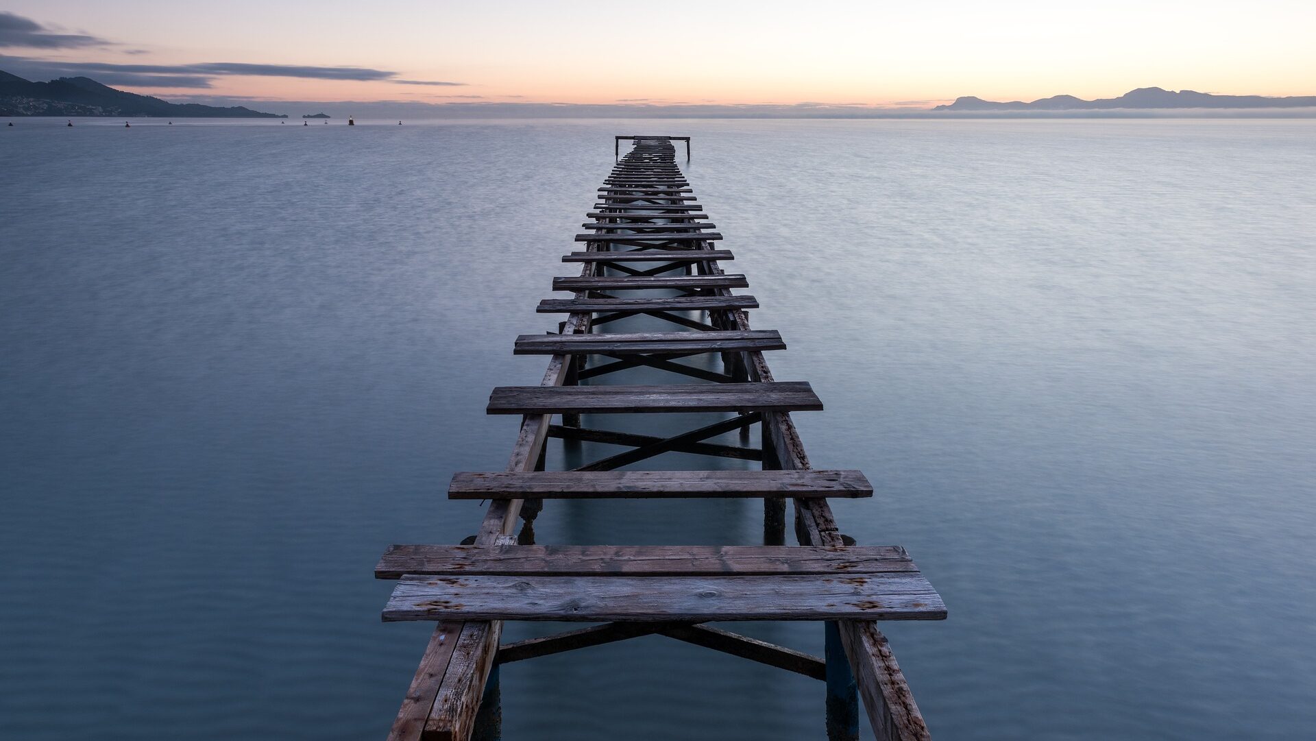 Wooden pier with missing planks over calm water.