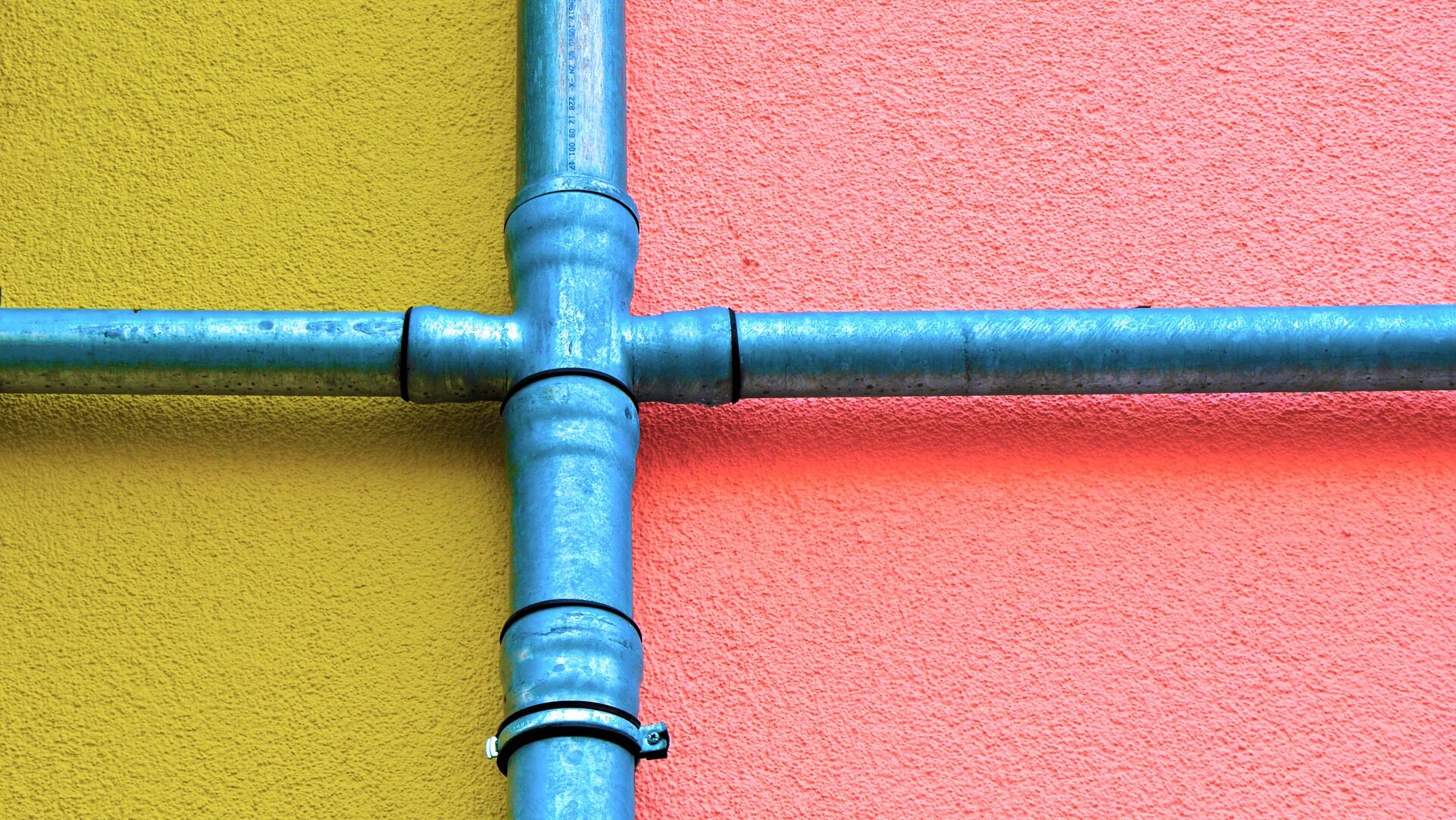 Four blue pipes joining together with a yellow and pink wall on each side