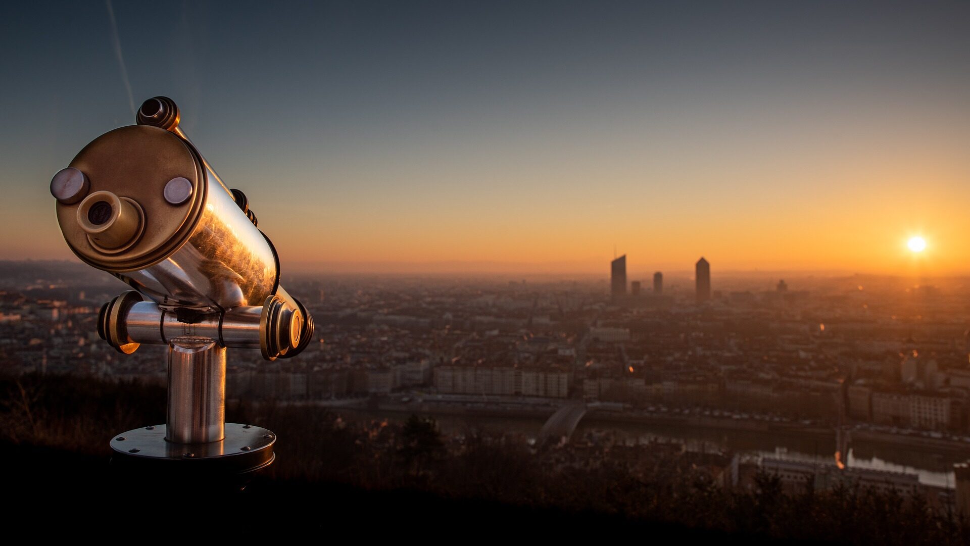 Telescope looking over a city skyline during sunrise.